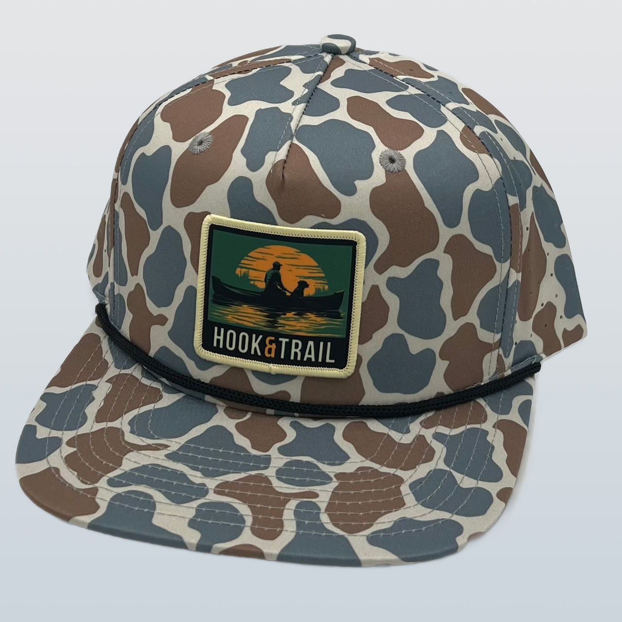  "Hook & Trail Canoe Patch Performance Cap in Blue Old School Camo, featuring a nostalgic camo pattern with vibrant blue tones. The cap showcases an embroidered canoe patch, symbolizing outdoor exploration. Made from moisture-wicking material for comfort and breathability, with an adjustable strap for a perfect fit. Ideal for outdoor enthusiasts seeking style and functionality in every adventure."