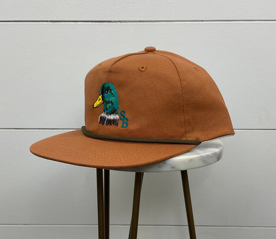 Terracotta-colored cap featuring a duck head emblem on the front, made from 100% cotton with a 550 paracord for durability. The mid-crown design, adjustable snapback, and one-size-fits-most feature make it a versatile and stylish accessory for various occasions.
