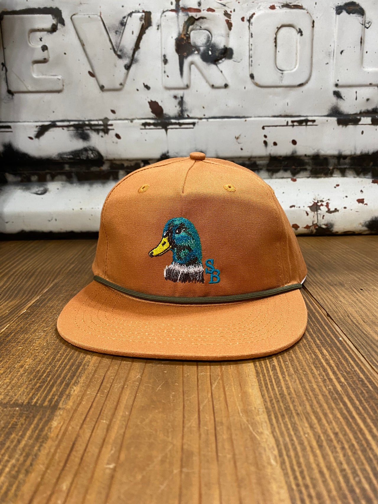 Terracotta-colored cap featuring a duck head emblem on the front, made from 100% cotton with a 550 paracord for durability. The mid-crown design, adjustable snapback, and one-size-fits-most feature make it a versatile and stylish accessory for various occasions.
